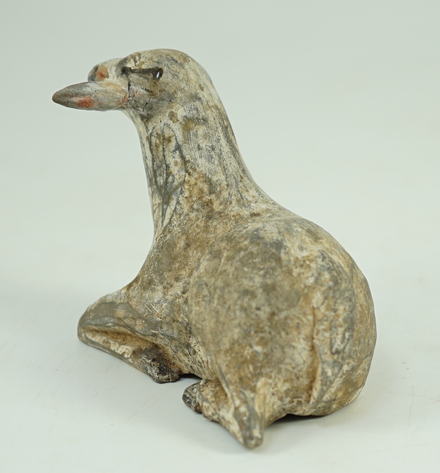 A Chinese painted grey pottery model of a recumbent sheep, Han dynasty, 10.2 cm long, One ear re-glued